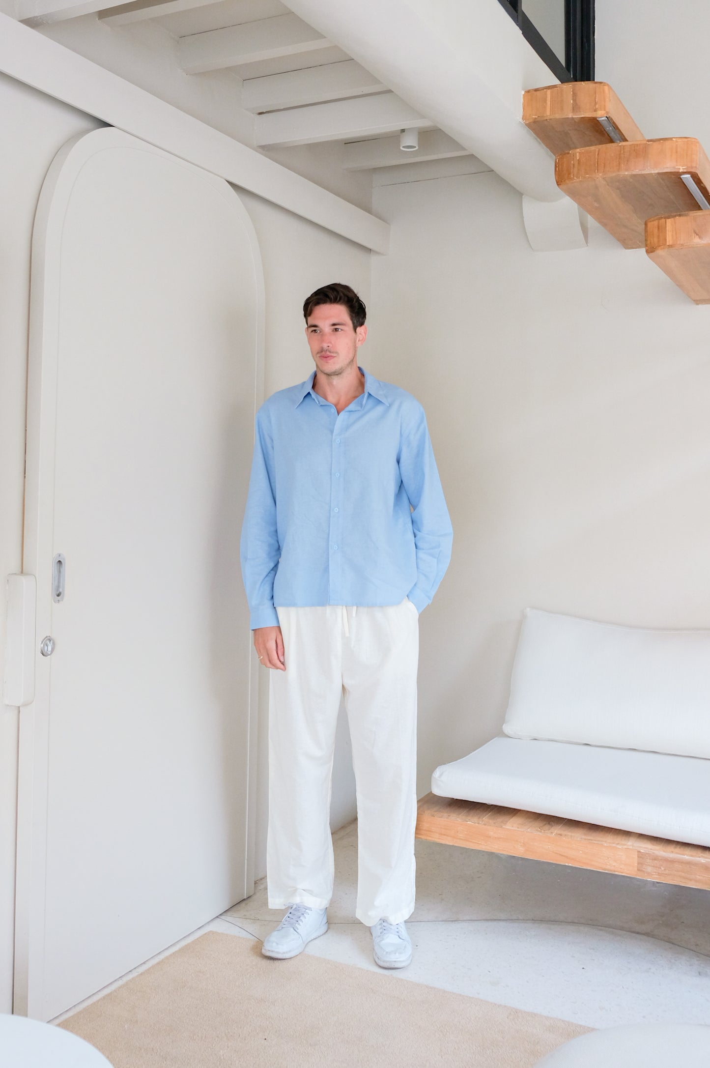 Man wearing minimalistic set of blue shirt and trousers made of linen captured in modern Bali style vila.