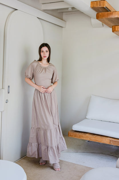 Model wearing linen long dress in beige colour by Una Linen Havn surrounded by white minimalistic interior.