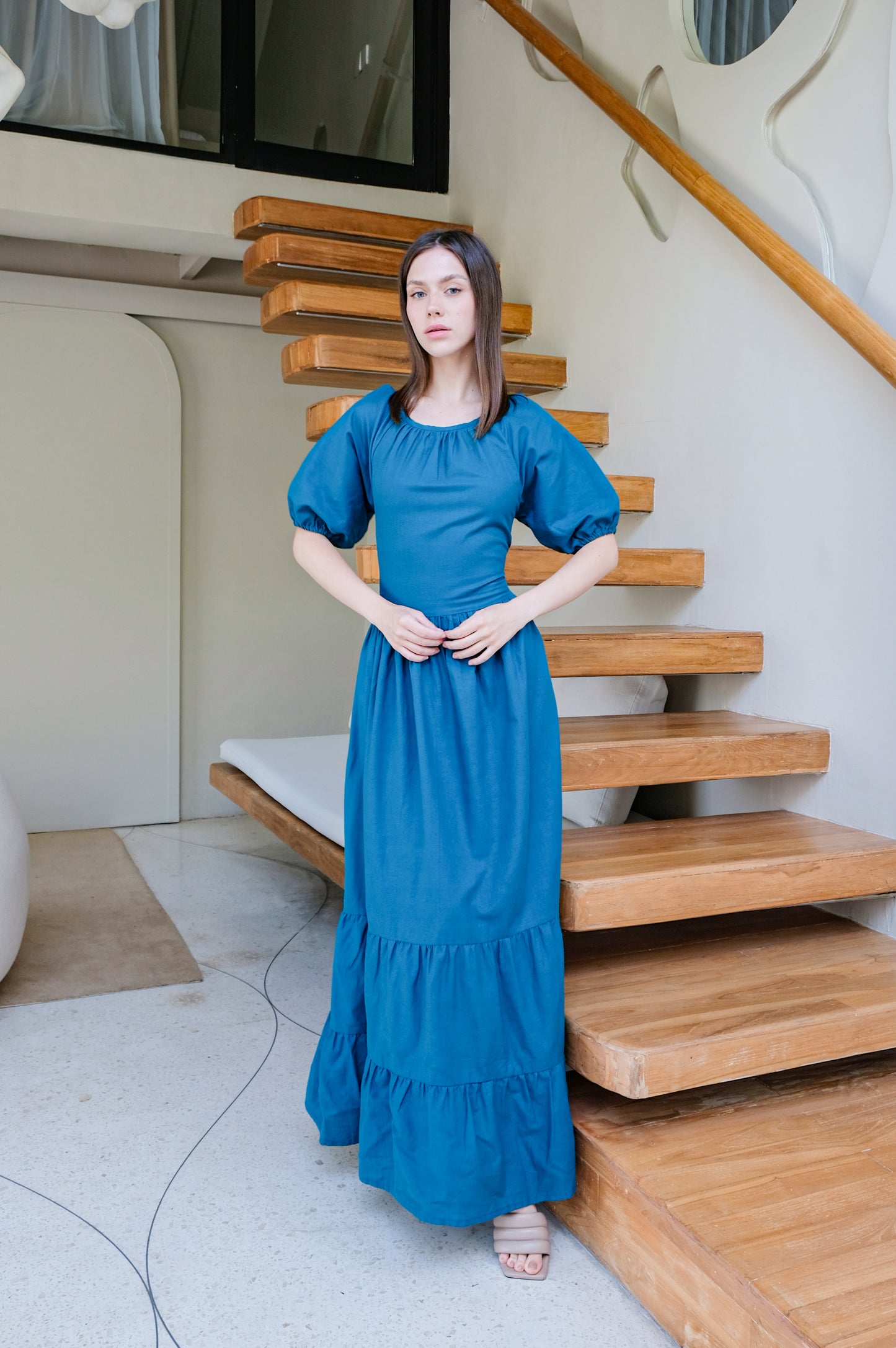Amalfi in blue linen long dress by brand Una Linen Havn with wooden stairs in background.